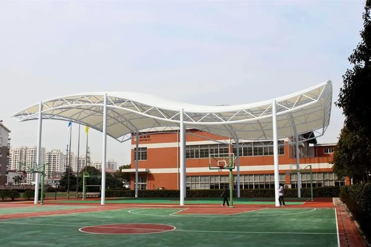 A basketball court covered by a steel canopy, featuring Playground tensile structures, designed by Shadeco
                                                    for enhanced outdoor play.